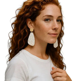 Woman wearing large white earrings on a plain background