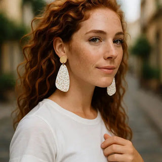 Woman wearing large, white, teardrop-shaped earrings outdoors.