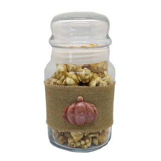 caramel popcorn in a clear jar with a hessian ribbon and orange pumpkin on a white background