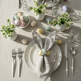 Easter table setting with pastel eggs, flowers, and a gray napkin on a light surface.