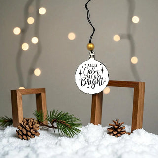 Decorative ornament with 'All is Calm, All is Bright' text on a snowy background with wooden frames and pine cones.