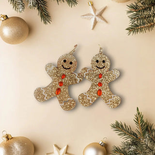 Gold glitter gingerbread man earrings on a beige background with Christmas decorations.