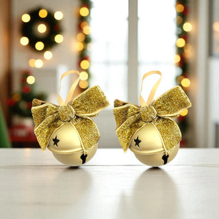 Two gold Christmas bells with glittery bows on a blurred festive background.