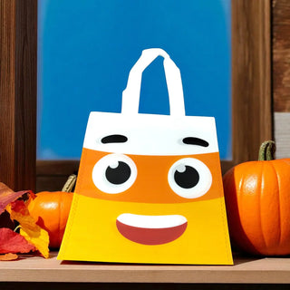 Halloween-themed candy bag with a face design on a wooden surface with pumpkins and leaves.