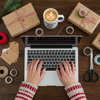 Laptop on a wooden table with Christmas gifts, coffee, and crafting supplies.