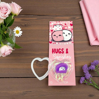 Pink packaging of 'Hugs & Squishies' with cartoon characters on a wooden surface with flowers.