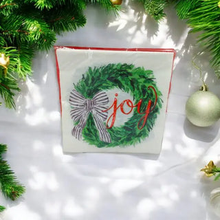 white serviette with green wreath adorned with a black-and-white bow and the word "joy"