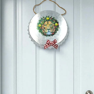 Decorative wall hanging with a lion's face, wreath, and red bow on a white paneled wall.