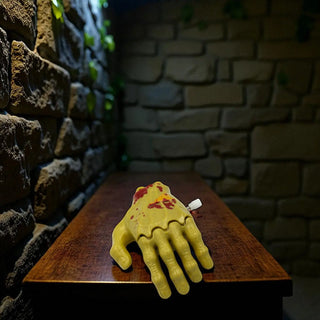 Yellow hand-shaped windup toyon a wooden board against a stone wall.