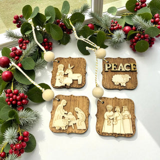 Wooden Christmas ornaments with nativity scene and 'Peace' design on a green leaf and berry background.