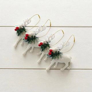 Set of white reindeer ornaments with red berries and greenery on a light wooden surface