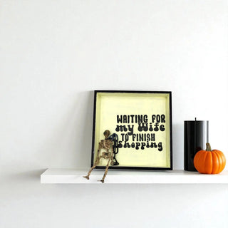 Framed artwork with skeleton and text on a shelf with a pumpkin and candle.