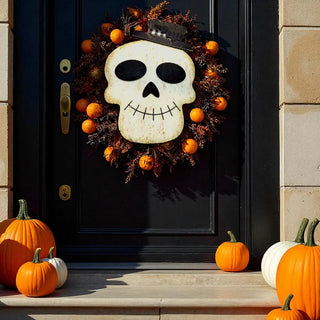 Decorative skull wreath on a black door with pumpkins around.
