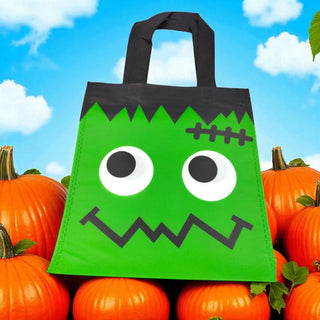 Green monster-themed tote bag with black accents on pumpkins against a blue sky.