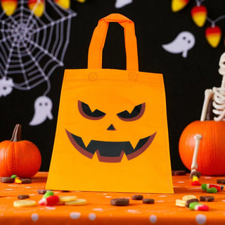Halloween-themed orange bag with jack-o'-lantern face design on a festive table with pumpkins and candy.