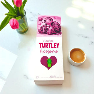 Card with turtle design and text 'You're Turtley Awesome' on a marble surface with flowers and coffee.