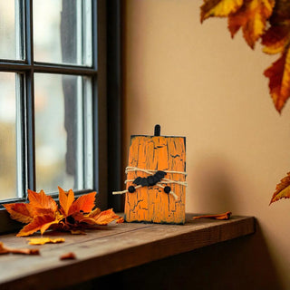 Small wooden pumpkin decoration on a windowsill with autumn leaves.