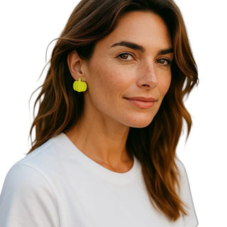 Woman wearing yellow pumpkin earrings on a white background