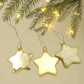 Three gold star-shaped ornaments hanging from a string against a beige background with greenery and lights.