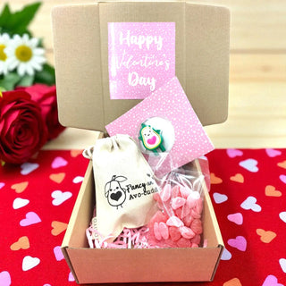 Valentine's Day gift set with pink heart-shaped candies, a small bag, and a card on a red heart-patterned surface.