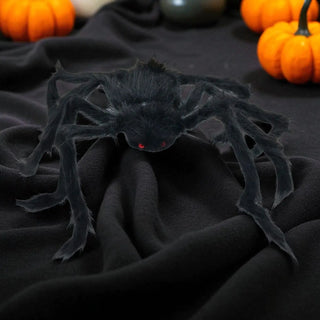 Black spider toy on a dark fabric background with pumpkins in the background