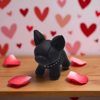 Black dog figurine on a wooden surface with red heart-shaped petals and a heart-patterned background.