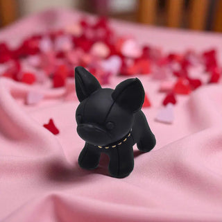 Black dog figurine on a pink surface with blurred red and white objects in the background