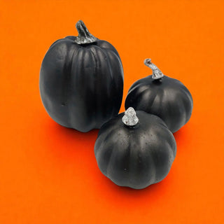 Three black pumpkins with decorative silver stems on an orange background