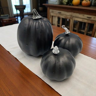 Three black decorative pumpkins with silver stems on a wooden table.