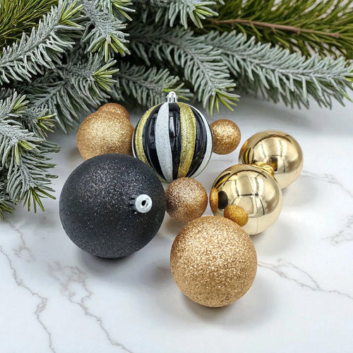 Decorative Christmas balls in gold, black, and silver on a marble surface with greenery.