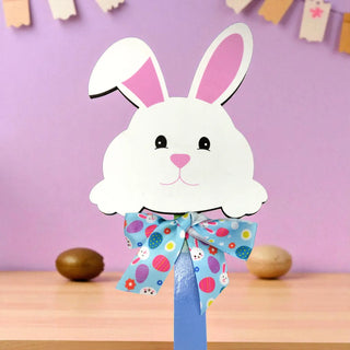 White paper bunny with a colorful bow tie on a wooden surface with a purple background