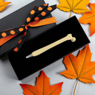 Decorative pen in a black box with an orange ribbon, surrounded by autumn leaves.