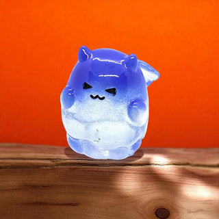 Glowing blue cat-shaped object on a wooden surface with an orange background