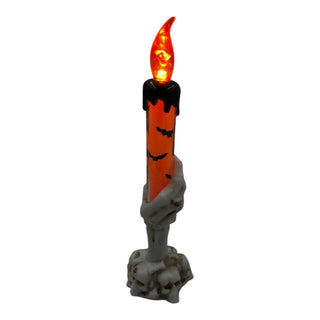 Halloween-themed candle held by a skeleton hand on a white background