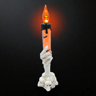 Halloween-themed candle with skeleton hand holding it against a black background
