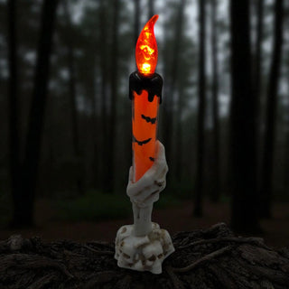 Halloween-themed candle with a skeleton hand holding it against a dark forest background