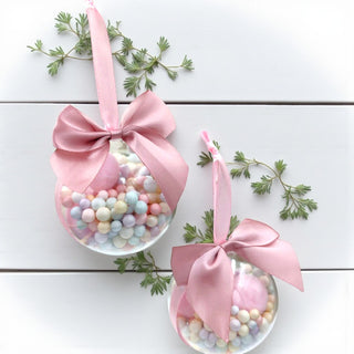 Two decorative ornaments with pastel beads and pink ribbons on a white wooden surface.
