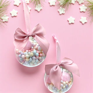 Two clear baubles with pink ribbons on a pink background with star-shaped cookies.