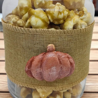 caramel popcorn in a clear jar with a hessian ribbon and orange pumpkin on a wooden background