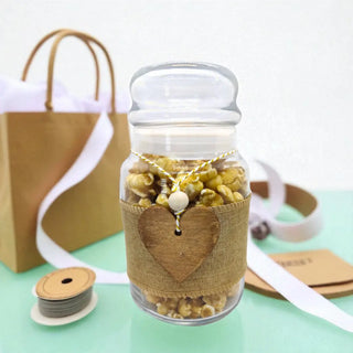 Glass jar with popcorn and a heart-shaped tag, tied with burlap ribbon, on a light green surface.