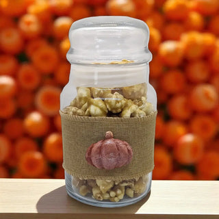 Glass jar filled with popcorn and a burlap sleeve with a pumpkin design against an orange background.