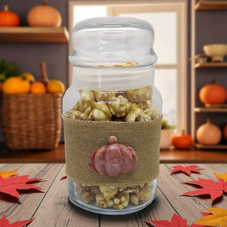 Glass jar filled with popcorn and a decorative pumpkin label on a wooden surface with autumn leaves.