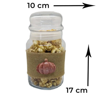 caramel popcorn in a clear jar with a hessian ribbon and orange pumpkin on a white background