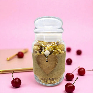 Jar with popcorn and a heart-shaped label on a pink background with cherries