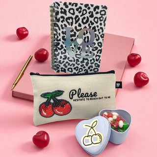 Leopard print notebook, pouch with cherry design, and heart-shaped container on a pink background