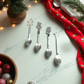 Set of silver spoons with Christmas-themed handles on a marble surface with festive decorations.