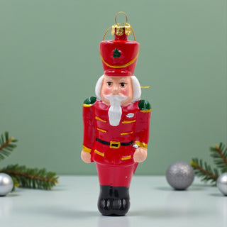 Christmas ornament of a red nutcracker soldier with a green background, traditional aesthetic