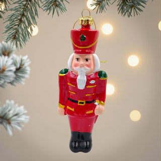 Red nutcracker Christmas ornament with a beige background and tree branches.