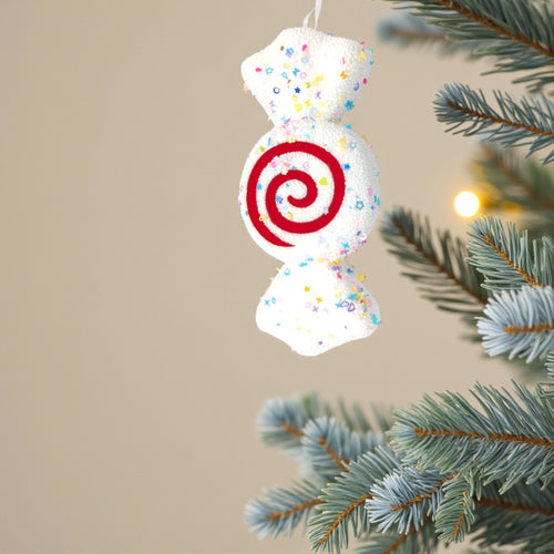 Confetti nougat candy ornament on frosted pine tree with warm fairy lights. Pastel Candyland Christmas decorating inspiration.