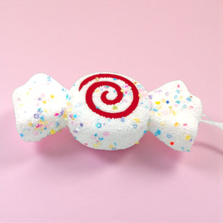 White candy-shaped Christmas tree ornament with colorful sprinkle details, photographed on a neutral background. Sweet shop holiday décor theme.